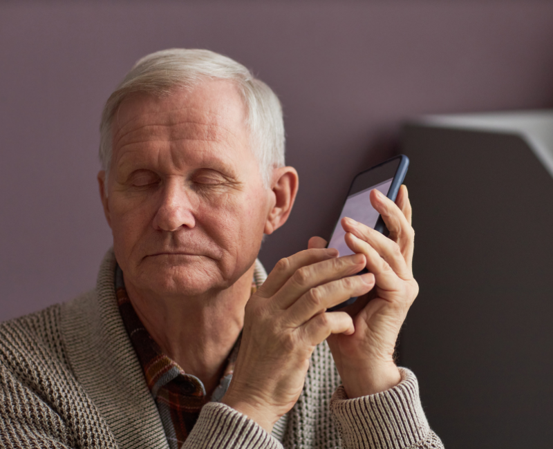 Senior man with blindness listening to an audio assistant on his phone